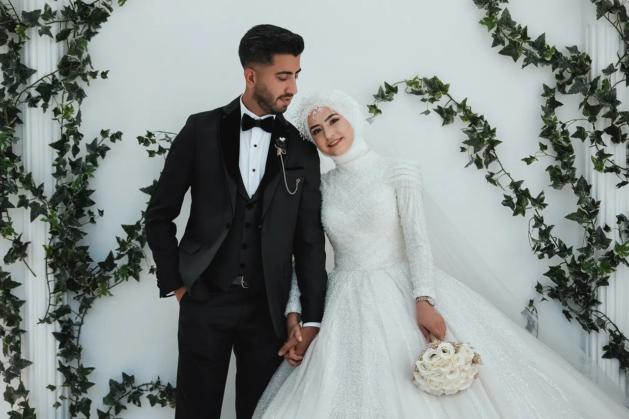 couple de mariés en tenue traditionnelle devant un mur fleuri